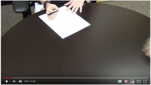 Hands on a table writing on a piece of white paper 