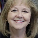 A white woman with mid-length blond hair and bangs smiles